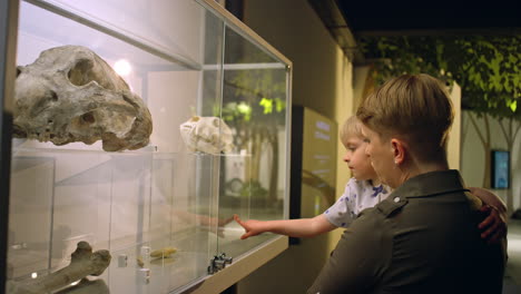 little girl in her mother arms looking at animal skeleton in a museum, side view