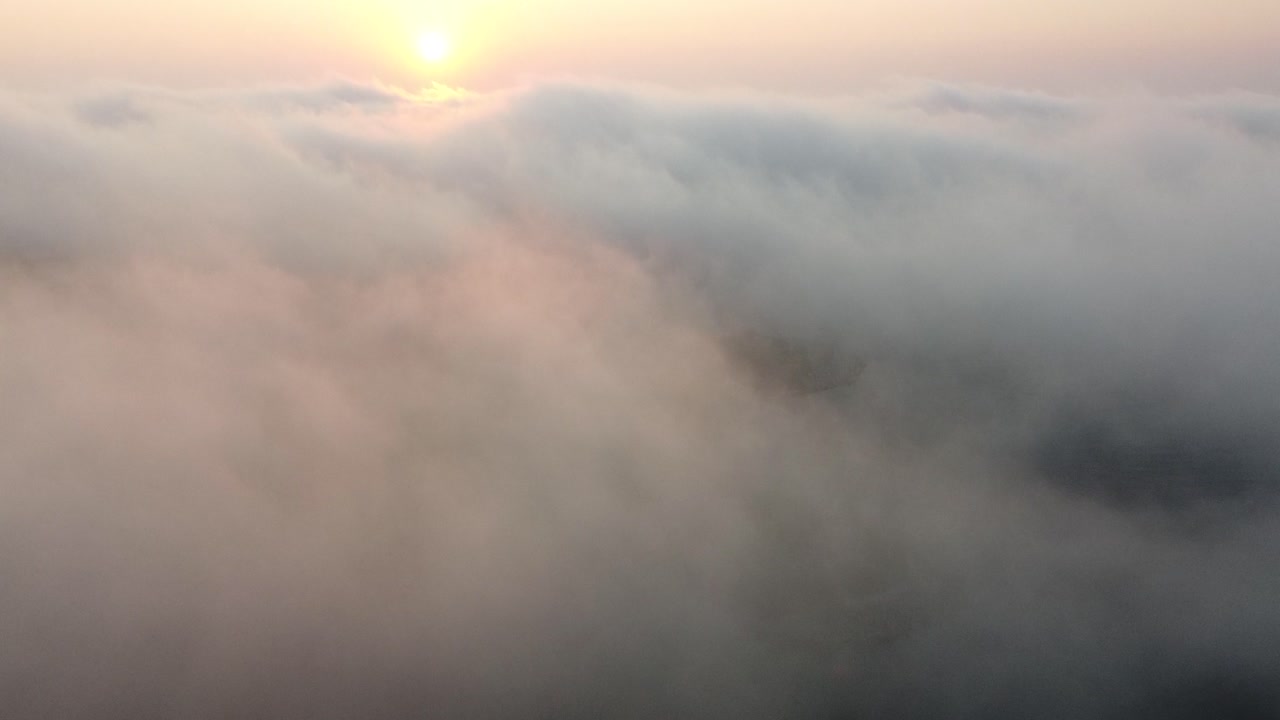 Aerial tilt up from limestone ground through fog revealing sunrise above misty clouds; 4k