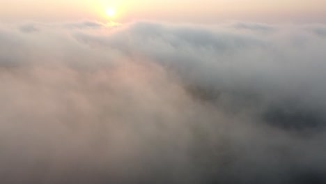 aerial tilt up from limestone ground through fog revealing sunrise above misty clouds; 4k