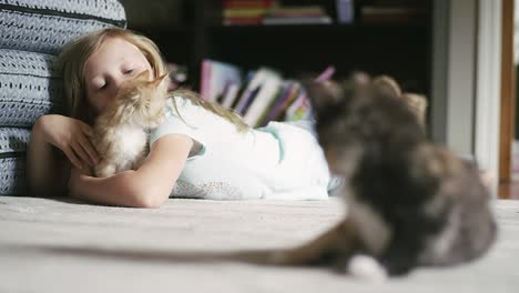 a little girl laying on the floor and petting a kitten, with another kitten in the foreground