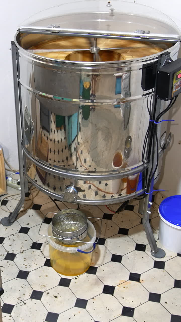 Little room in the apiary for harvesting honey. Electric machine extractor working in the corner. Few buckets are filled with freshly removed honey. Vertical video
