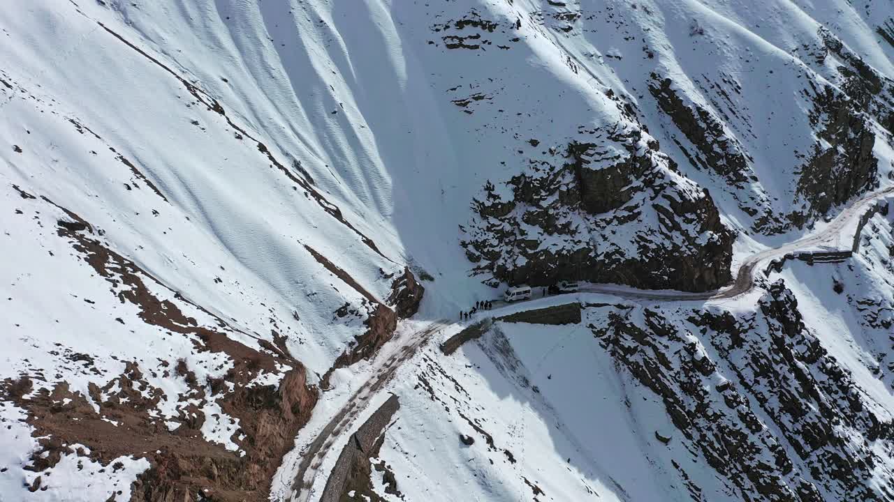 Aerial shot of group of travelers stuck in the middle of road due to snow road block in winter spiti revealing huge landscape of himalayas