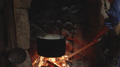 Woman-raking-buring-logs-in-flames-below-cauldron-in-stone-fireplace