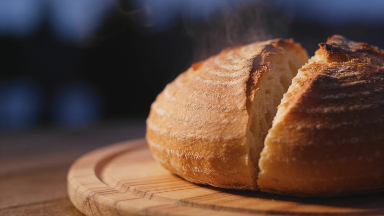 Steaming freshly baked crusty loaf with top cut cooling on wooden board, sending rising steam