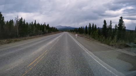 pov - driving on the alaska highway in the yukon territory; driving thru boreal forests with mountain peaks and teslin lake visible in the distance; concepts of wilderness, adventure, and travel