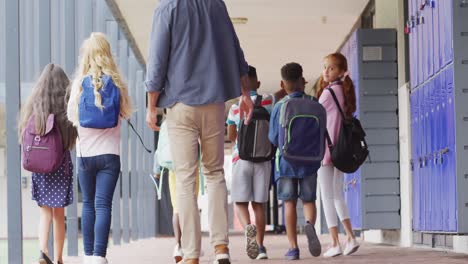 Vielfältiger-Männlicher-Lehrer-Und-Glückliche-Schulkinder,-Die-In-Der-Schule-Spazieren-Gehen