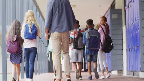 diverse male teacher and happy schoolchildren walking at school