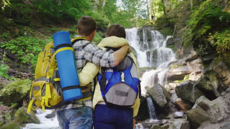 a young couple of tourists admire the waterfall they stand in an embrace the back view 4k 10 bit vid