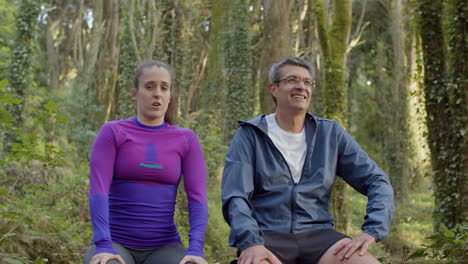 man and woman sitting and resting after trail running in forest