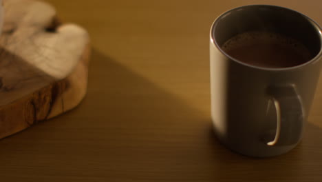 close up of person putting down steaming cup of hot chocolate drink on table