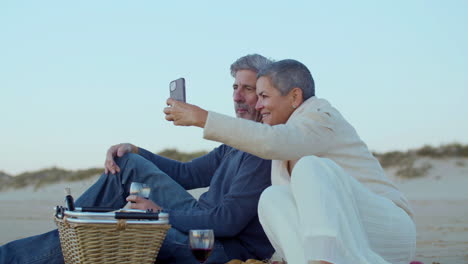 feliz pareja caucásica tomando una foto selfie mientras hace un picnic en la playa