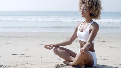 woman meditating on beach in lotus position