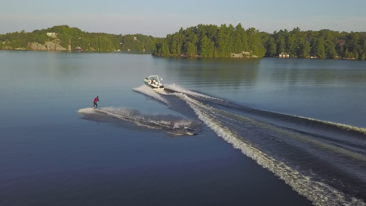 Wakeboarder fliegt akrobatisch über die Heckwelle eines Motorboots auf einem ruhigen See.
