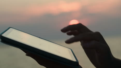 woman with pad by sea at sunset