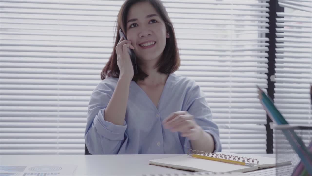 아름다운 미소 짓는 젊은 아시아 여성은 집에서 거실에 앉아있는 동안 노트북에서 일합니다. 아시아 사업가 여성은 집 사무실에서 일하기 위해 전화를 사용합니다. 집에서 시간을 즐기고 있습니다.