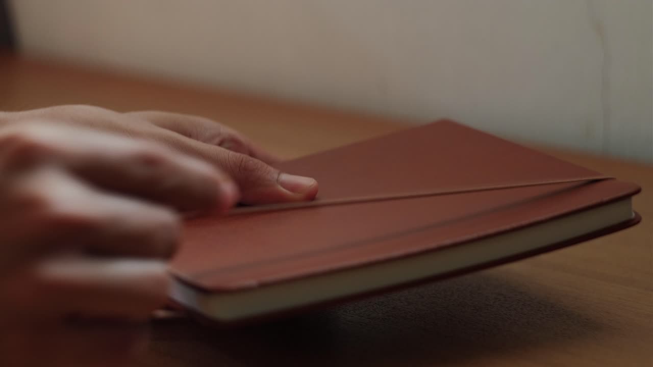 Static close-up shot of hand flipping through journal notebook pages and closing it at quiet workspace