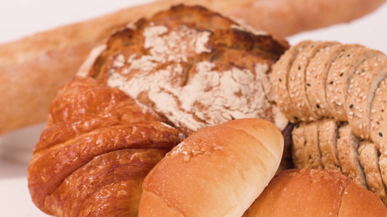 Close-up shot of hands picking fresh bread from a diverse bakery assortment on white background.