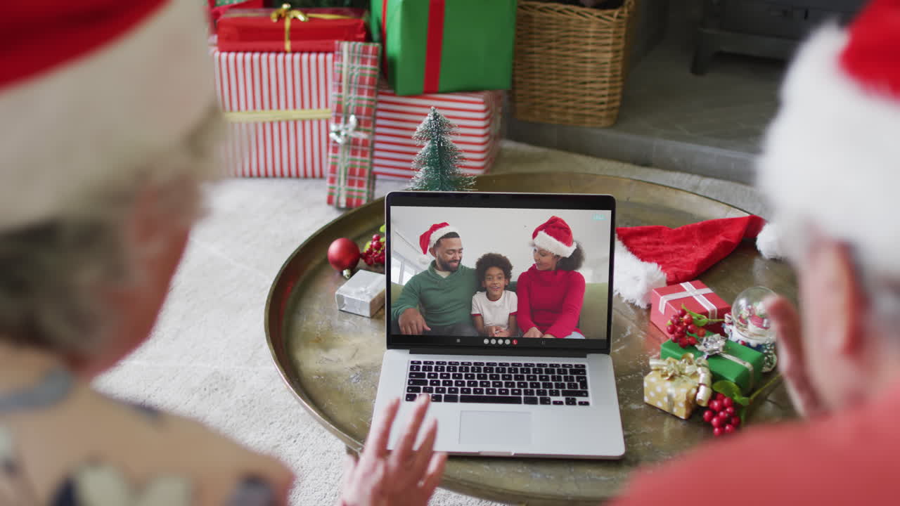 pareja caucásica mayor con sombreros de santa usando computadora portátil para una videollamada de navidad con la familia en la pantalla