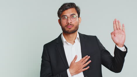 indian man raising hand to take oath, promising to be honest and to tell truth keeping hand on chest