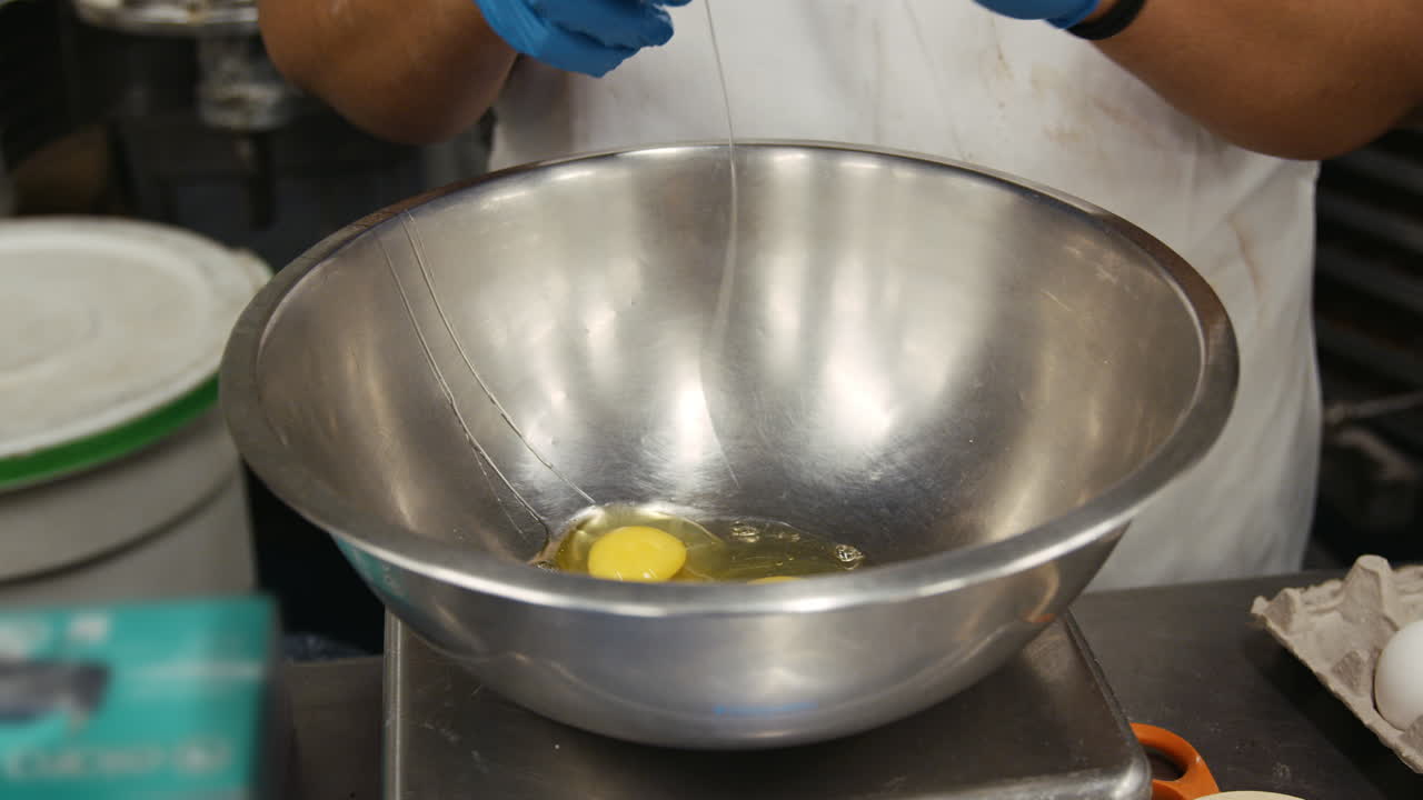 Baker breaking eggs into a mixing bowl, mid section