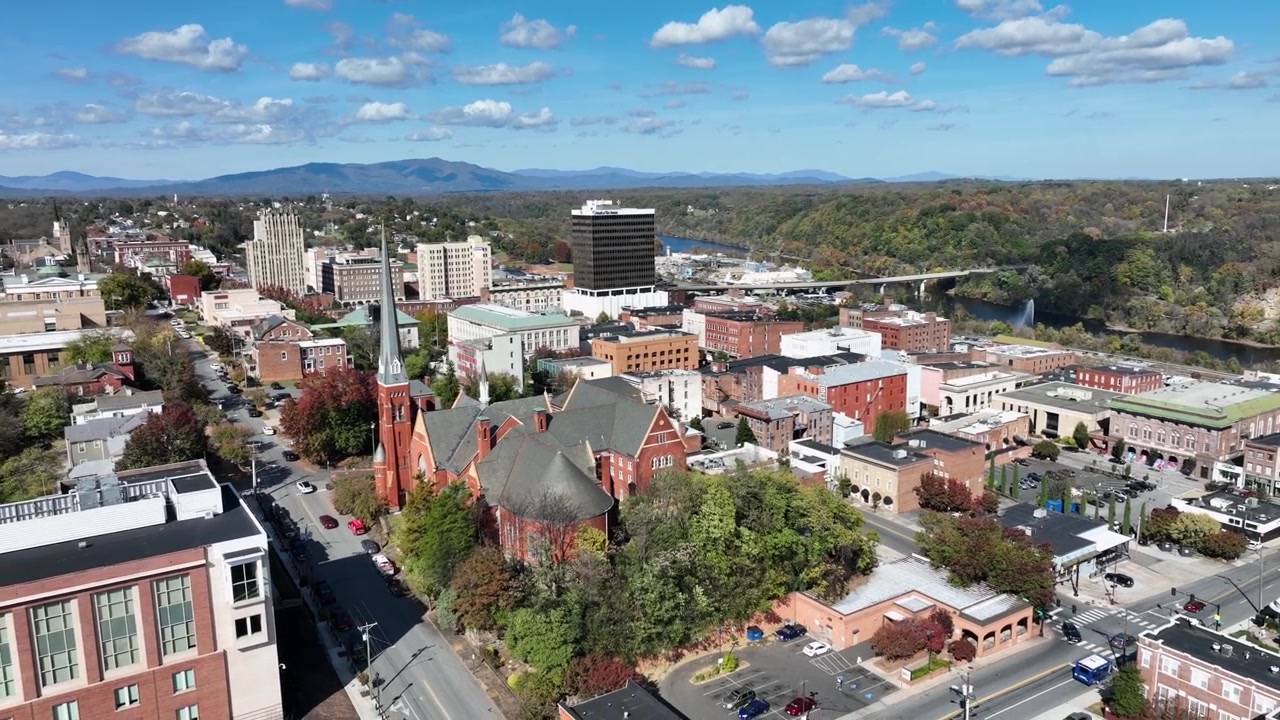 Iglesia histórica en un pueblo estadounidense con el idílico paisaje verde de Virginia. Día soleado con montañas y un río caudaloso en la ciudad. Toma aérea amplia con dron ascendente.