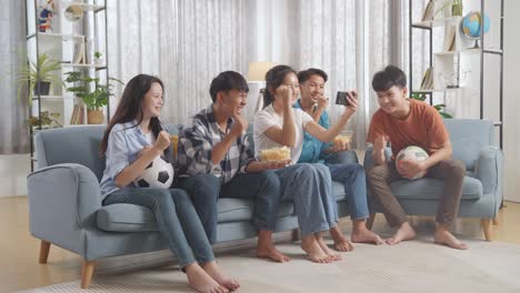 asian teenagers cheering and watching football game on smart phone and celebrating victory at home