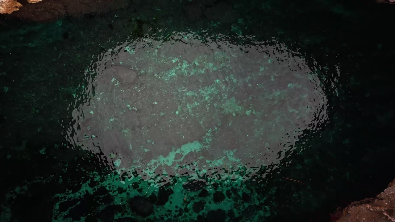 Dron zachycuje vertikální pohled shora dolů na zářivě tyrkysovou vodu uvnitř mořské jeskyně Coral Lagoon v Mellieze na Maltě, orámovanou ostrými vápencovými útesy.