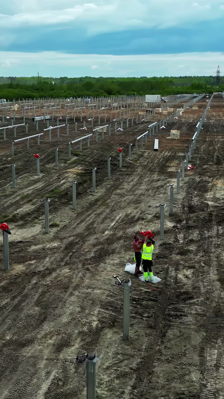 Vertical View Of Solar Power Plant Construction With Workers Installing Steel Poles. Aerial Shot