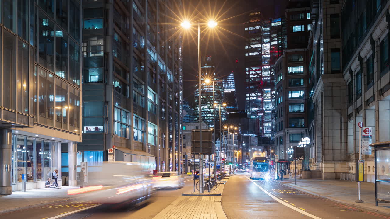 Night time lapse of a busy road in London, UK with cars and buses zooming past and skyscrapers skyline in the background