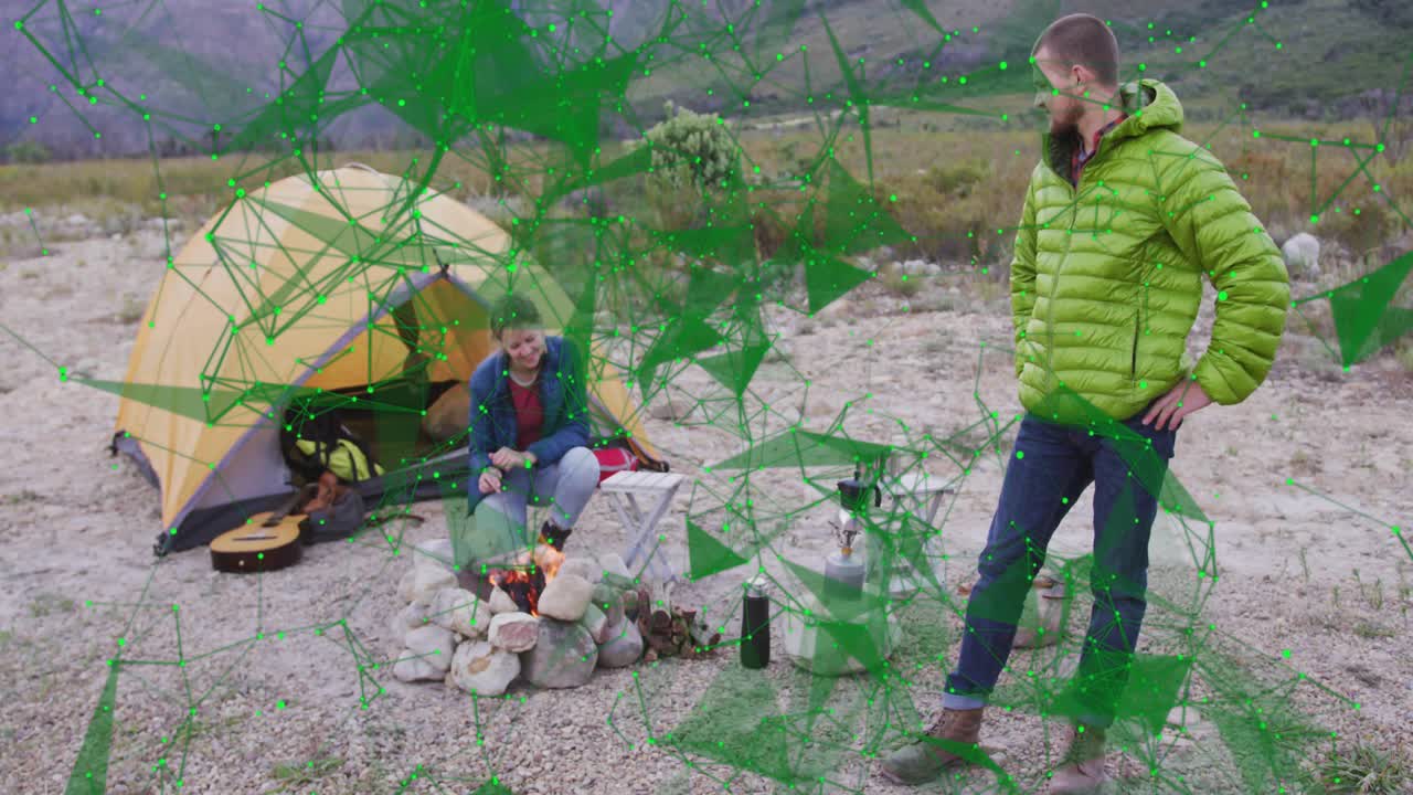 Man and woman igniting campfire on riverbed then brewing kettle on camp stove under cloudy sky