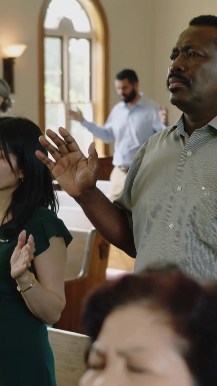 Vertical video: Praying elder woman mouthing as worship starting in church pews, raised hands