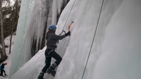 a woman climbing a frozen cliff face using ice axes