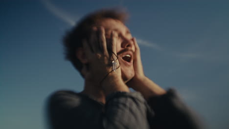 man covering his face with hands under a blue sky