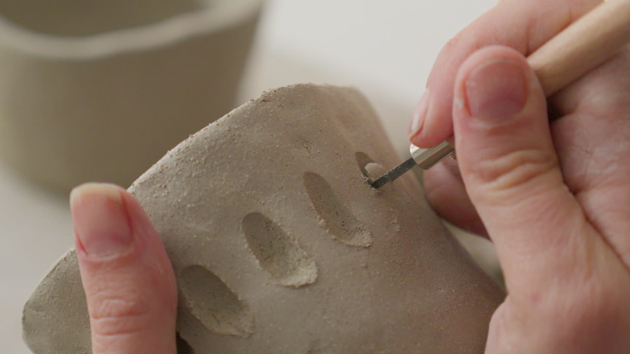 Engraving intricate designs into soft clay with a specialized tool, showcasing artisan's delicate touch