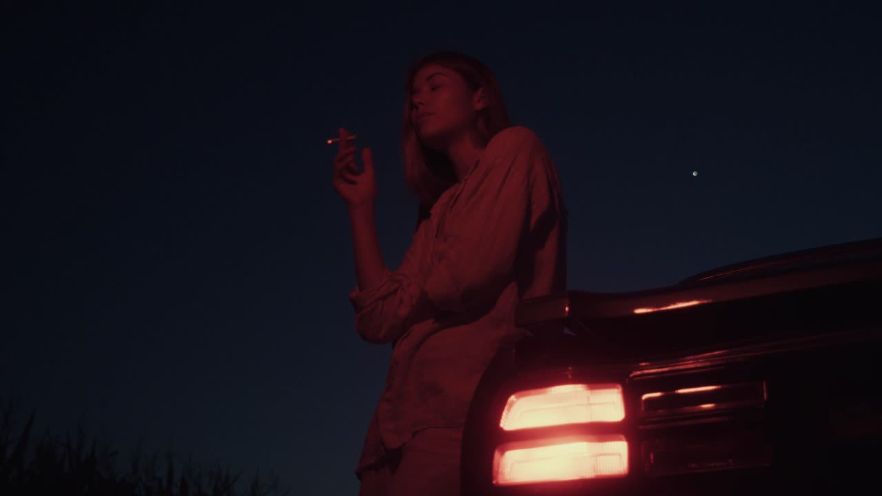 Donna che fuma accanto all'auto di notte