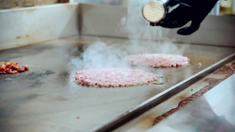 4K-Kinoaufnahmen-Eines-Kochs-Beim-Zubereiten-Und-Kochen-Eines-Köstlichen-Hausgemachten-Burgers-In-Einer-Restaurantküche-In-Zeitlupe,-Indem-Er-Die-Burger-Würzt