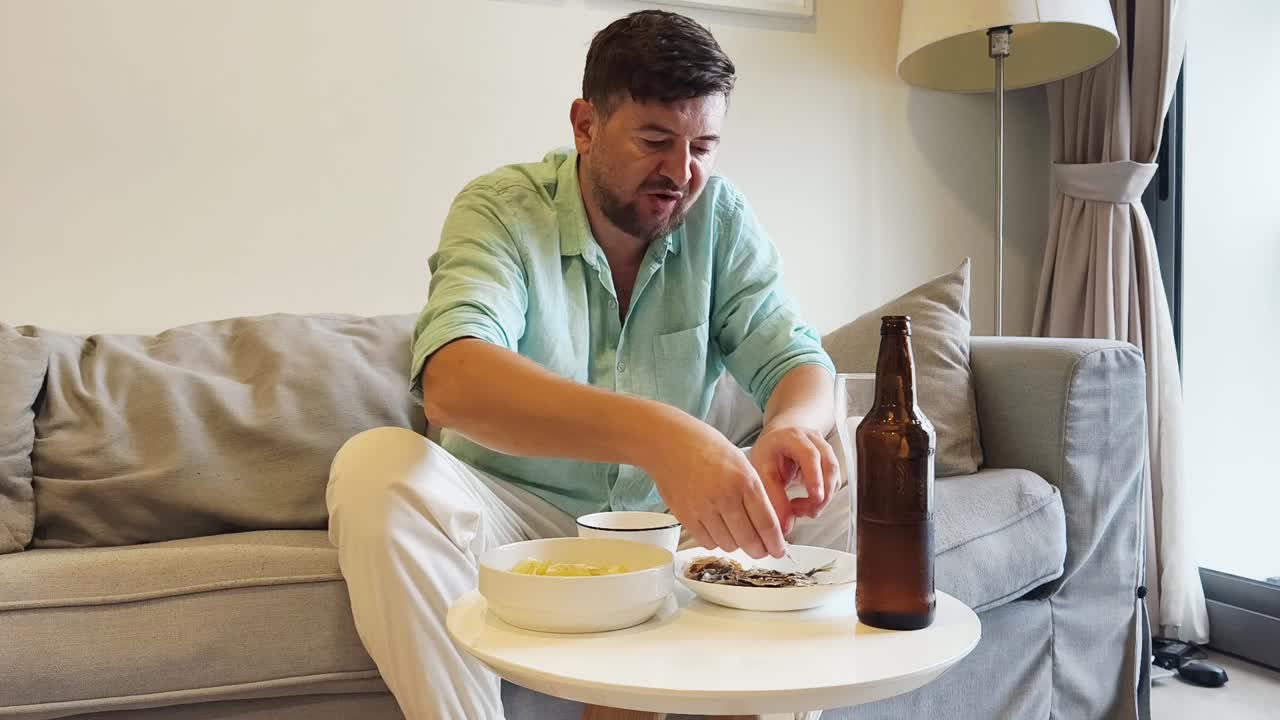Man eating and drinking beer on a sofa at home