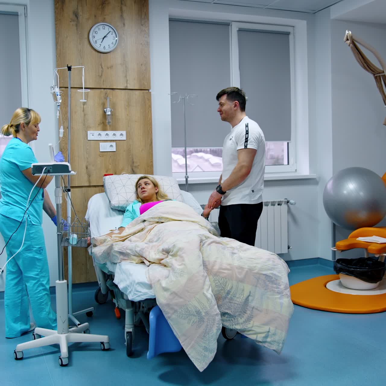 Pregnant lady lies in hospital bed. Nurse attaches drop counter to woman's hand. Husband stands beside soothing his wife