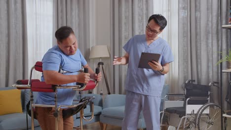 side view of asian male nurse with a tablet talking to a patient standing in a walker about medical test results during a physical therapy at home