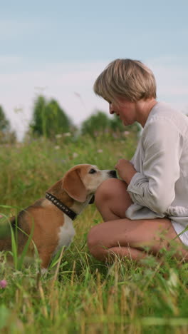 dog owner interacting playfully with her pet dog as they share a tender moment in grassy field, owner is squatting down while dog gazes up and appears to be taking something from her hand
