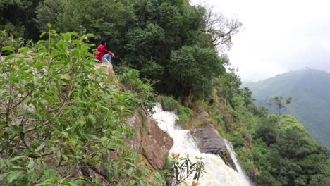 hombre sentado en un acantilado mirando una cascada