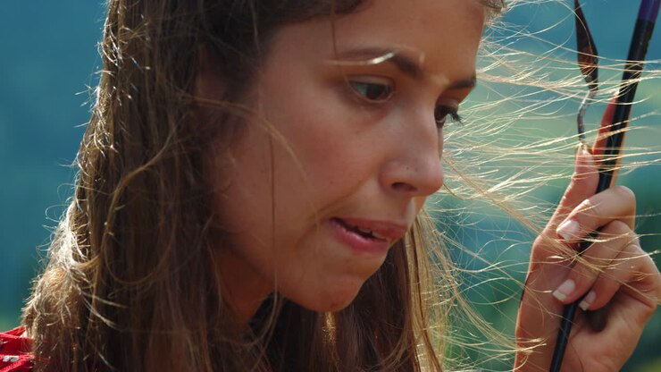Creative painter biting lip windy day. Closeup girl holding paint tools in hand