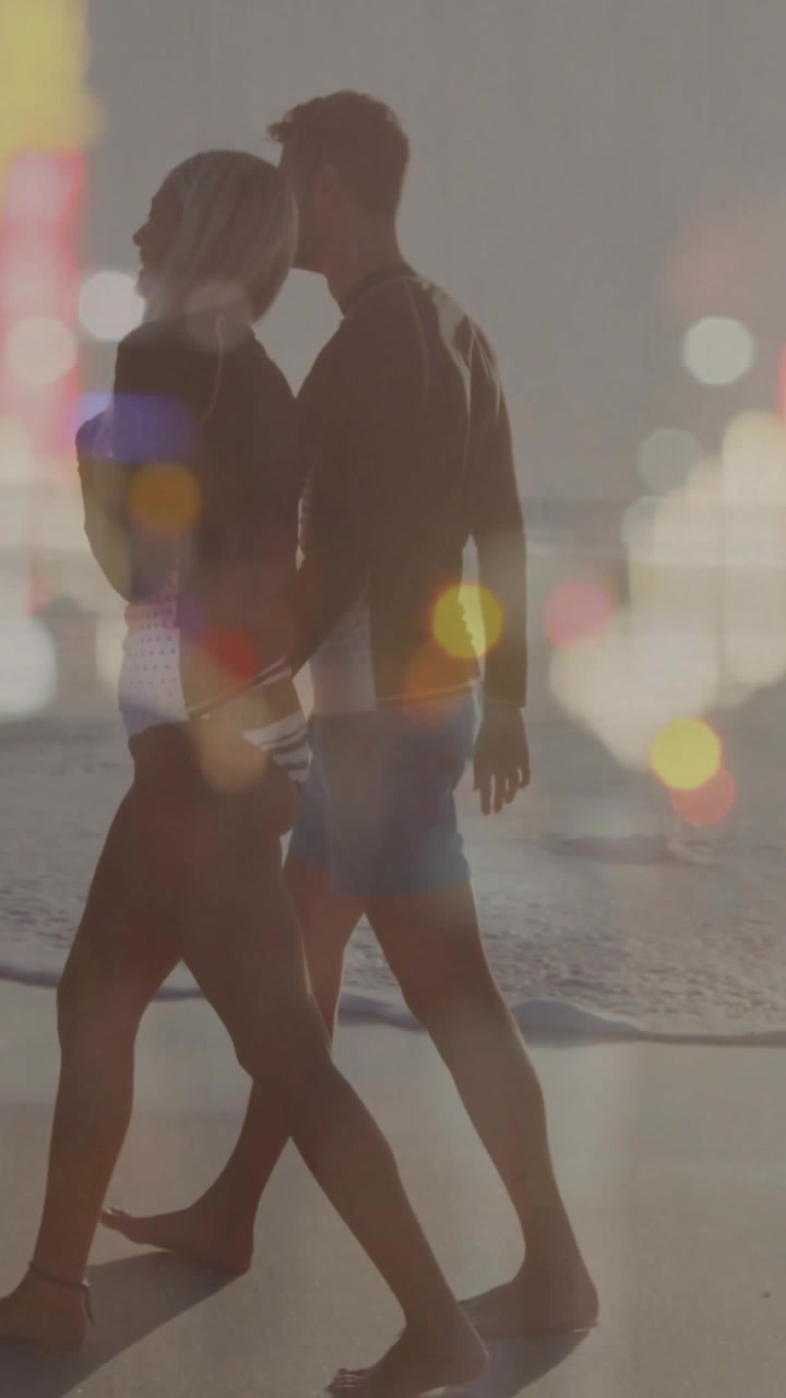 Video verticale: Donna che cammina sulla riva, uomo che entra e si unisce, bokeh che incornicia una passeggiata al tramonto in viaggio.