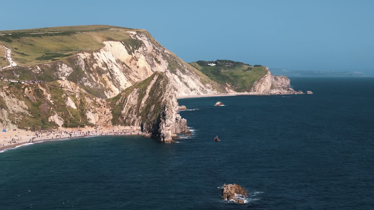 Circle left around Durdle Door with cliffs and green fields above