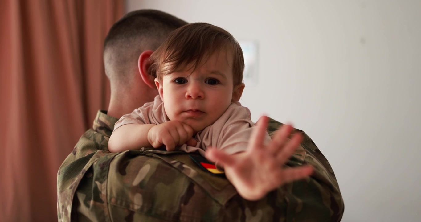 Bambino carino che guarda la fotocamera mentre è tenuto in braccio da un soldato