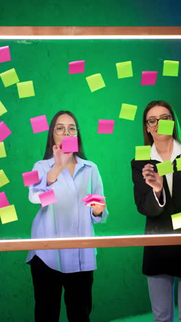 two female office workers put stickers on the glass board. project planning, organization, innovation. vertical video.