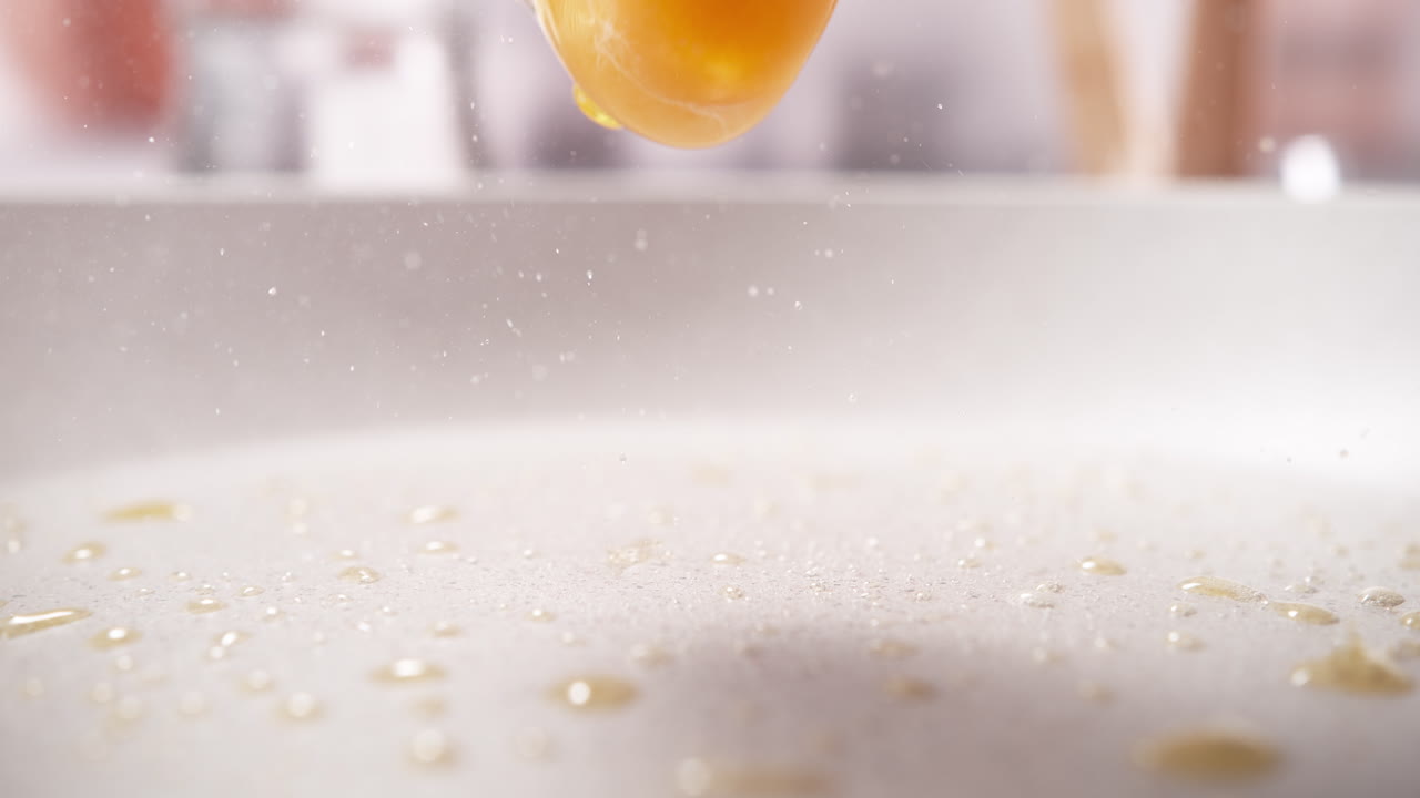 Cracked Egg Falls Into The Skillet With Hot Sizzling Fat, Making A Splash in Macro and Slow Motion