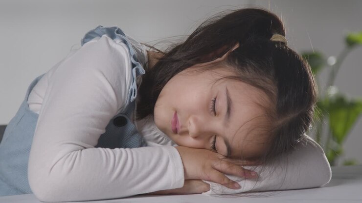 Toma de estudio de niña cansada durmiendo con la cabeza apoyada en la mesa y con fondo blanco 1