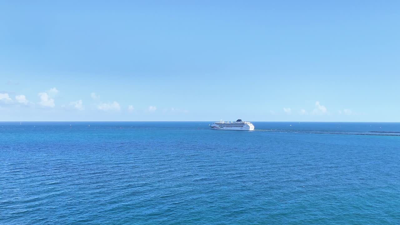 드론이 마이애미 항구에서 대서양으로 출발하는 크루즈 선박을 포착하여 선박이 은 파란 바다에서 항해하는 것을 보여줍니다.