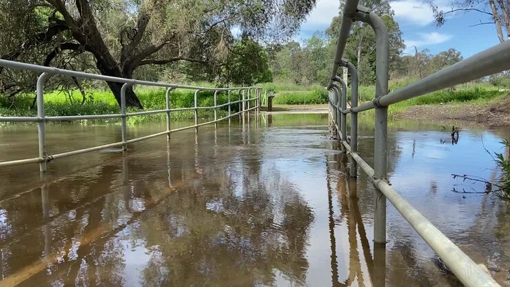 Inquadratura dal basso che attraversa un ponte pedonale allagato su un ruscello ingrossato a seguito di piogge torrenziali e inondazioni durante le alluvioni australiane nell'ottobre 2024.